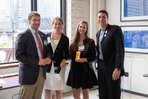 CLRC Director Stephanie Fajuri stands in a row with three other people, all facing the camera and smiling. Stephanie holds her 40 Under 40 Award.