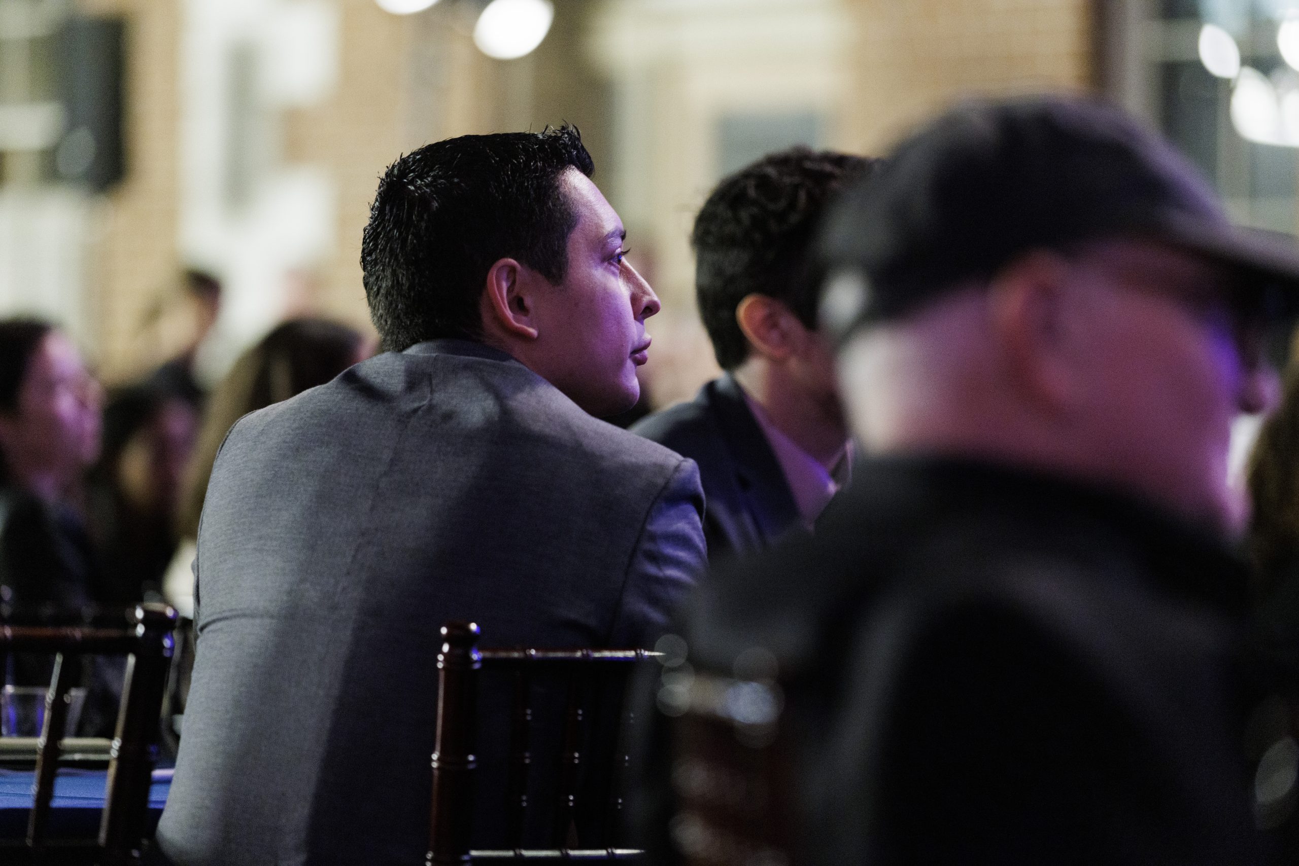 Candid shot of audience member with cropped haircut and suit, pursed lips, leaned forward, listening