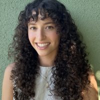 Sophie Tohl head shot--Sophie wears a ribbed white blouse, pendant necklace, and dark curly hair