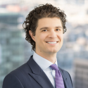 Giovanni Saarman Gonzalez head shot - Giovanni wears a dark suit, white shirt, and purple tie