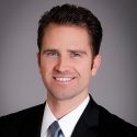 Matthew Summers wears a white shirt, blue tie, and black suit against a gray background