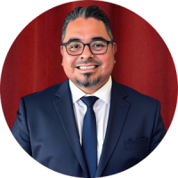 Lucio Rodriguez wears a navy blue tie and suit, glasses, and short black hair for his head shot
